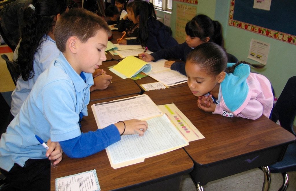 Two students work together at a desk within an elementary classroom.