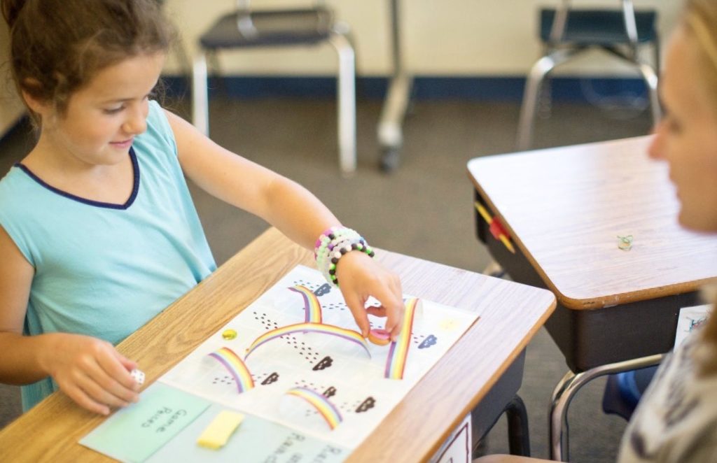 An elementary aged student is playing a literacy game with her teacher.