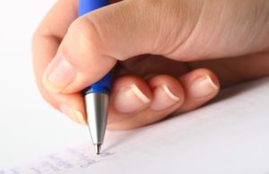 Close up of a hand holding a pen over white paper.