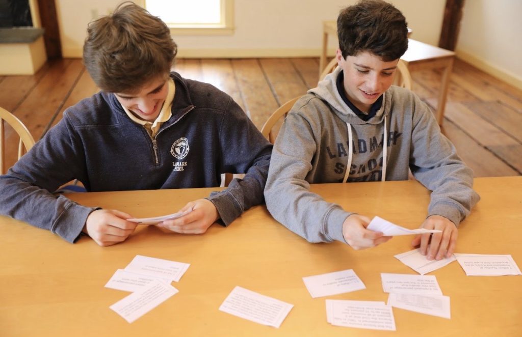 Two high school students seated side by side at a desk reviewing flash cards.