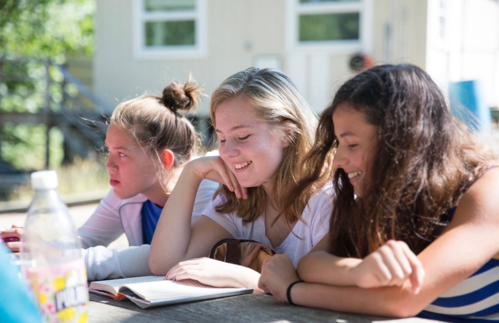 Three students sitting outside sharing a book.