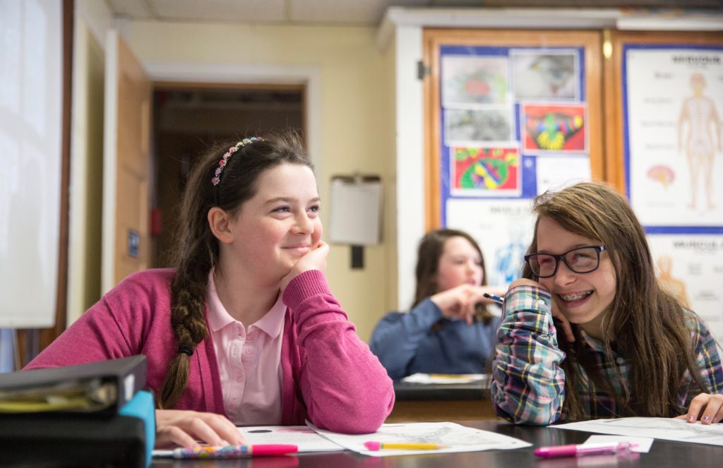 Two middle school students smiling at a desk within a science classroom.