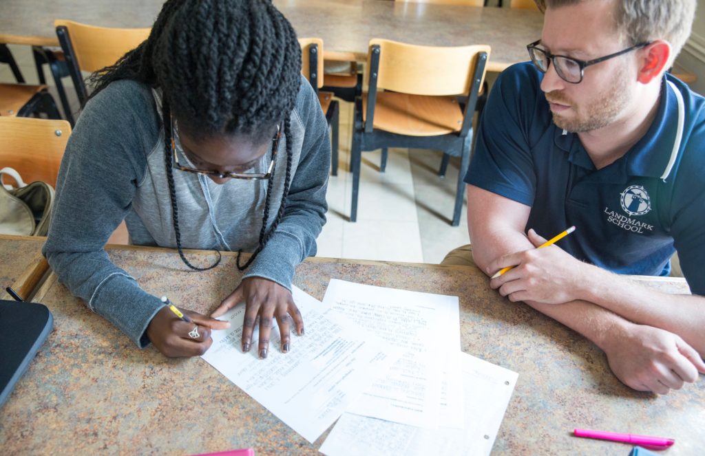 A high school student and a teacher seated side by side to work on writing together.