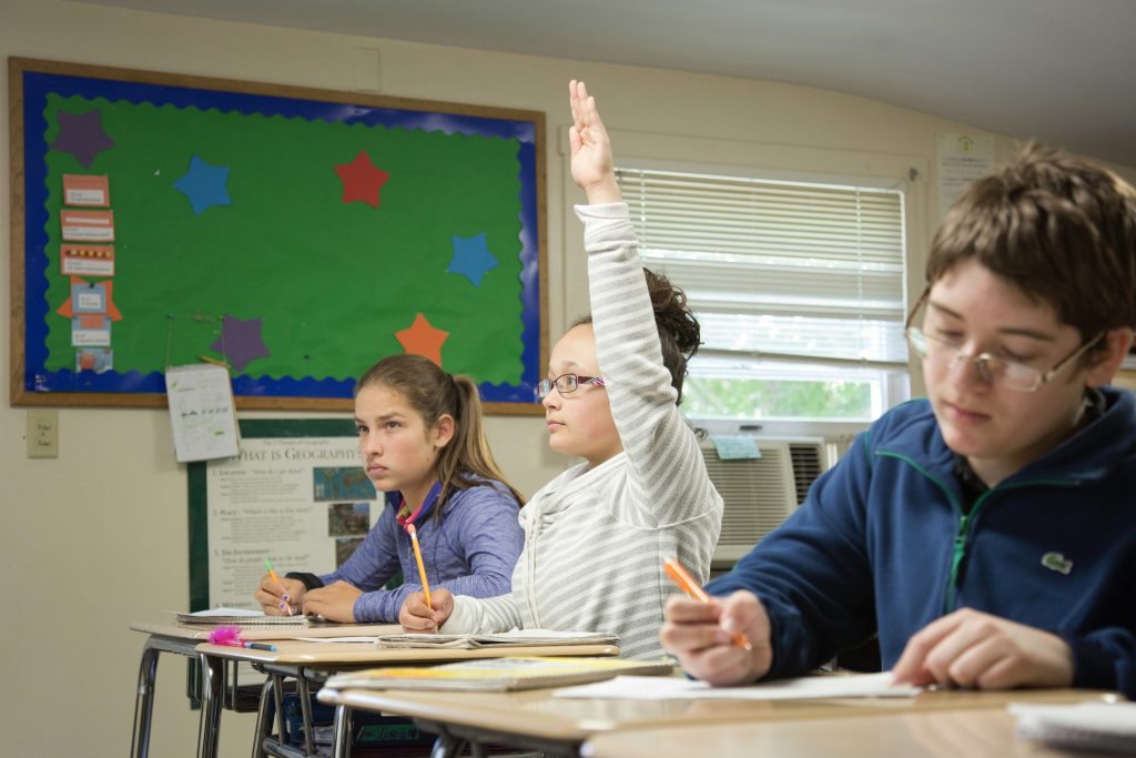 Student raising hand in the front of a classroom.