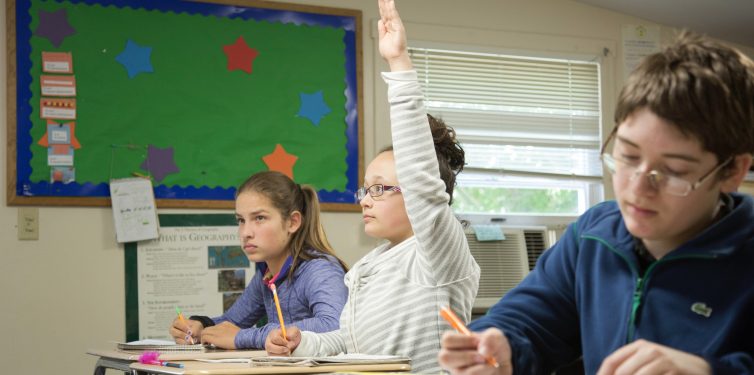 Student raising hand in the front of a classroom.