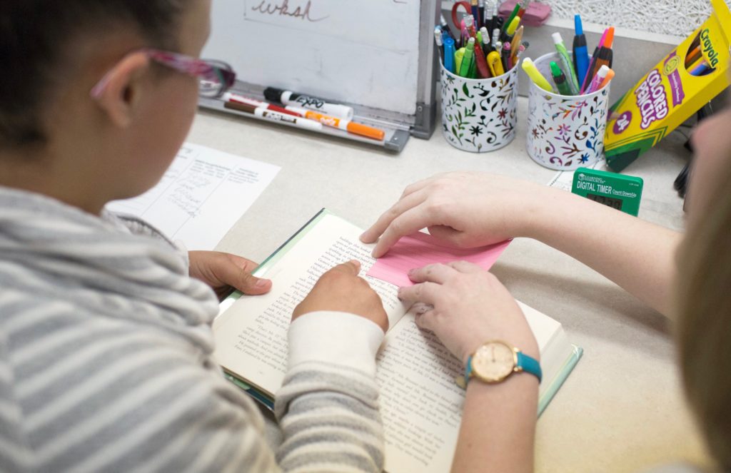 Student and teacher working collaboratively on reading a book. The student is tracking position with her finger.