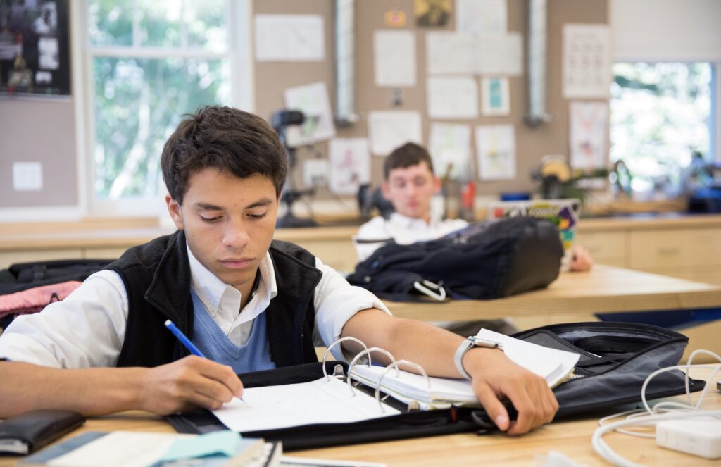 A high school student is focused on writing notes in a binder.