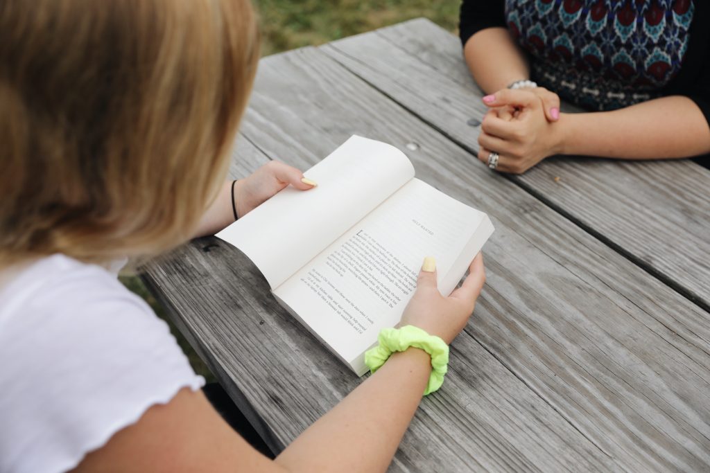 Bird's eye view of student reading a book sitting at a picnic table with adult sitting across from them.