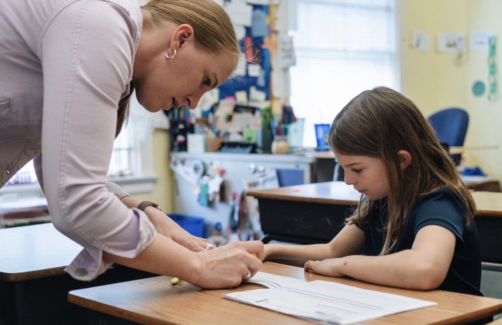 An elementary teacher helping a student with an assignment at the student's desk.