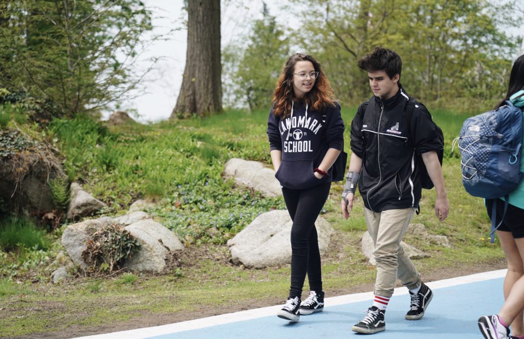 Two high school students chatting while walking outside between academic buildings.