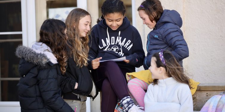 5 students gathered around a notebook outside smiling. The photo illustrates students having fun at school!