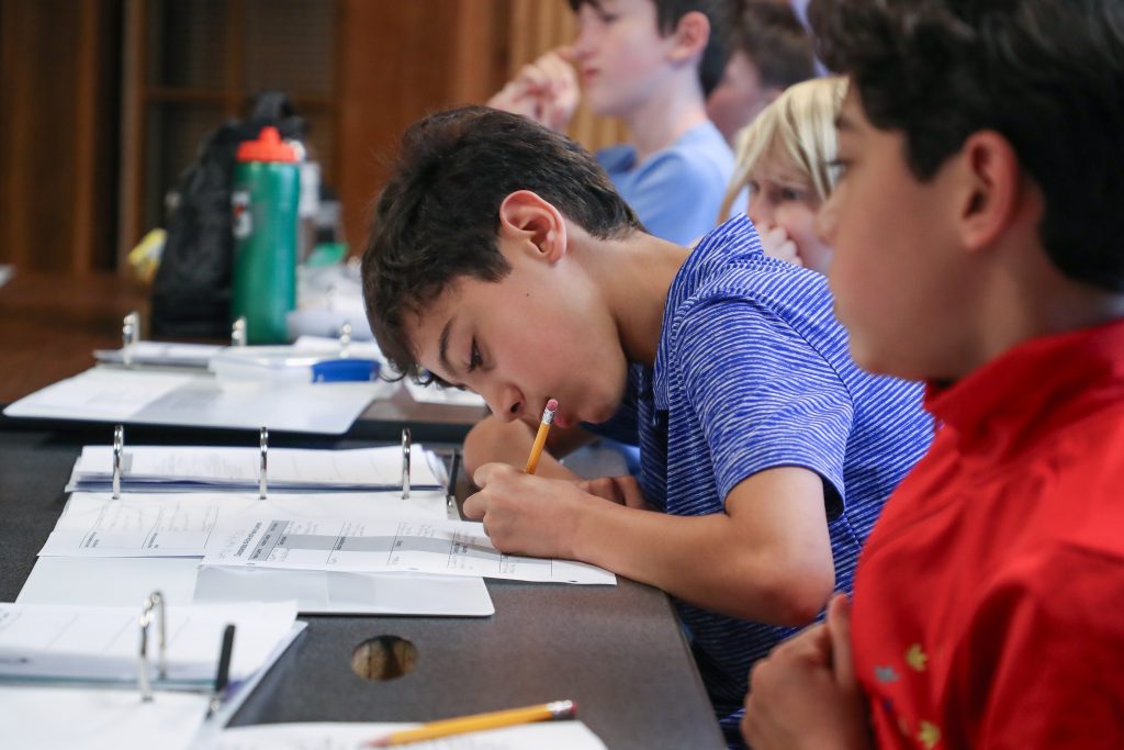 Student leaning over desk taking focused notes with paper and pencil.