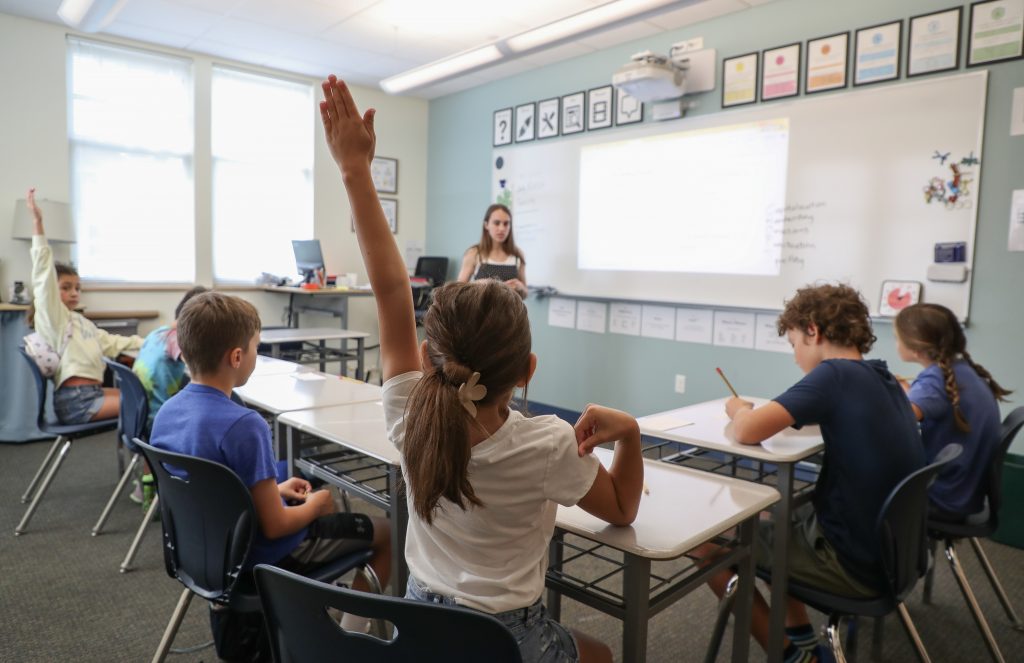 Student raising her hand in a small elementary/middle school classroom.