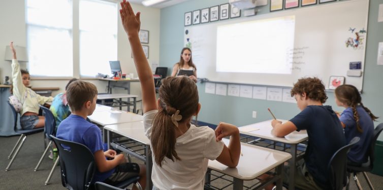 Student raising her hand in a small elementary/middle school classroom.