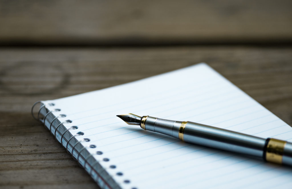 Open spiral notebook with a pen resting on top.