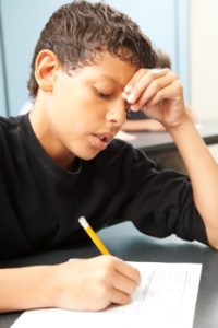 A student looks frustrated while writing with a pencil.